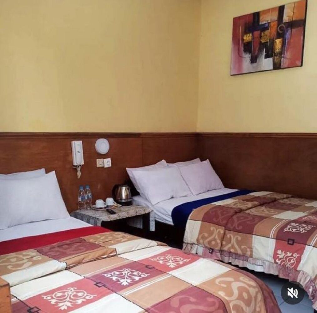 A hotel room with two beds, a wooden headboard, a bedside table with a phone and a kettle, and a painting on the wall.