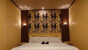 Una cama bien hecha con sábanas blancas y cabecera de madera, flanqueada por paneles verticales de madera y un papel tapiz estampado.