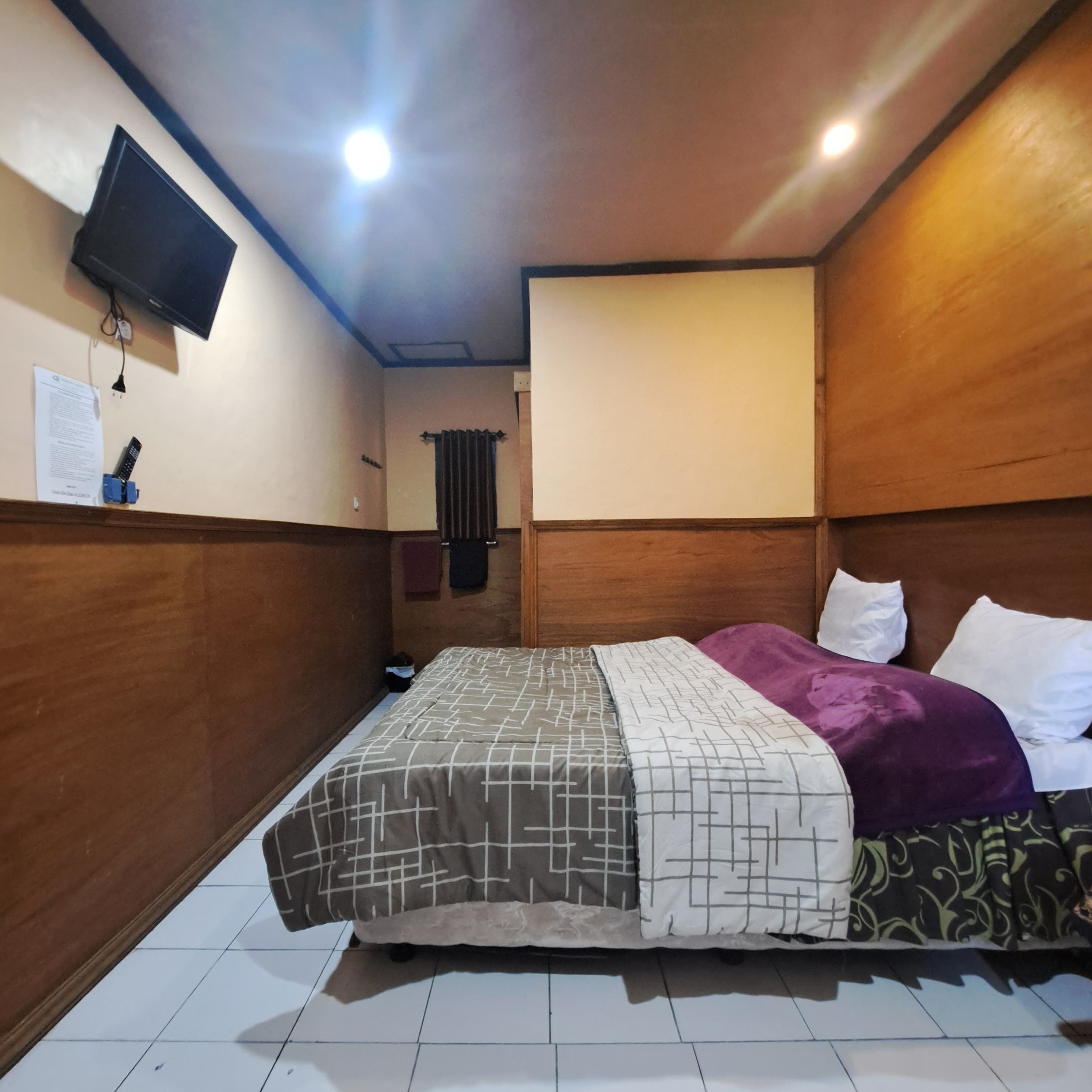 A small, compact bedroom with a bed, a television mounted on the wall, and a radiator.