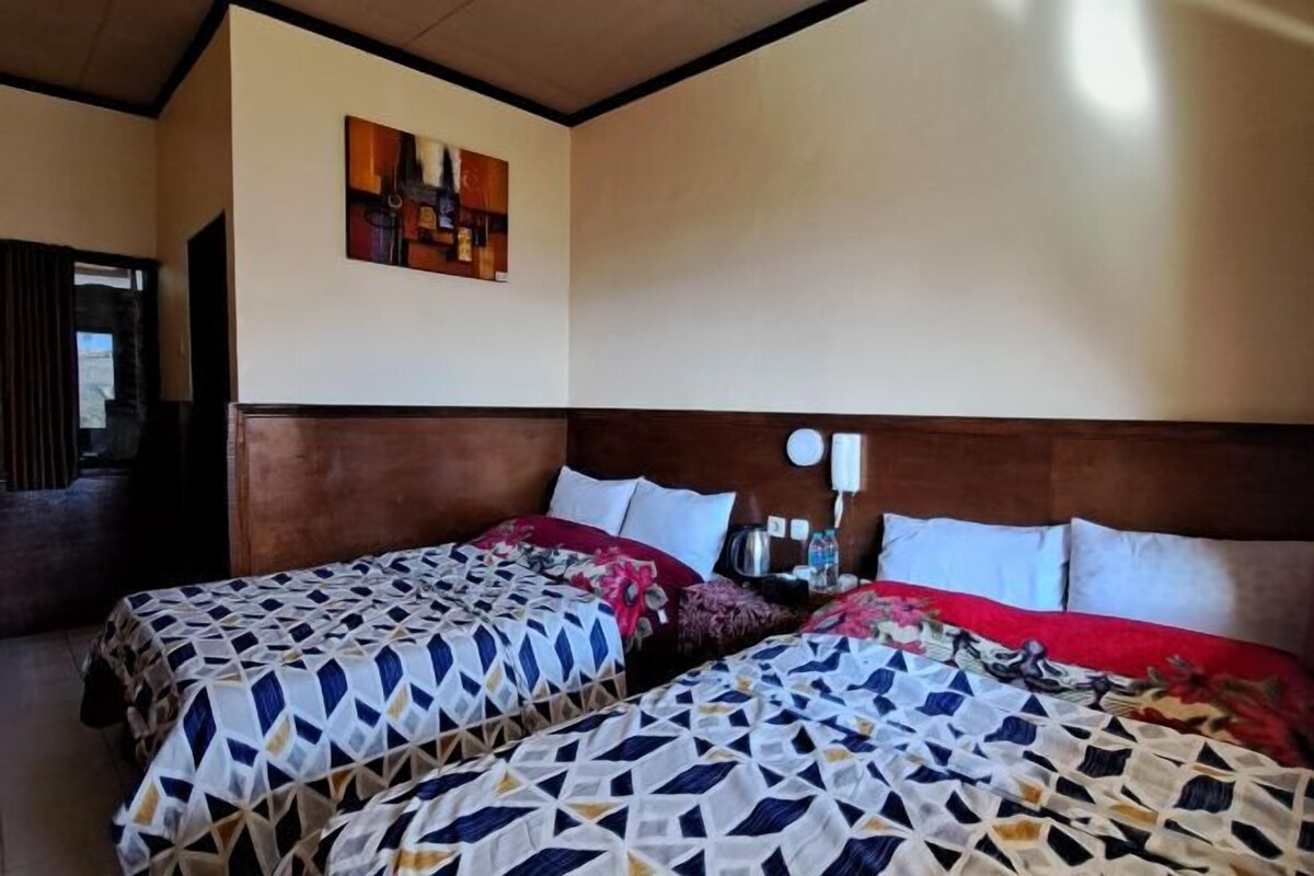 Habitación de hotel con dos camas, cabecero de madera, una obra de arte colgada en la pared y una mesita de noche con lámpara.