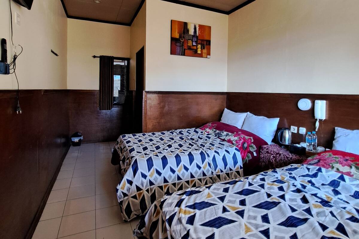 A hotel room with two beds, a painting on the wall, and a wooden headboard.