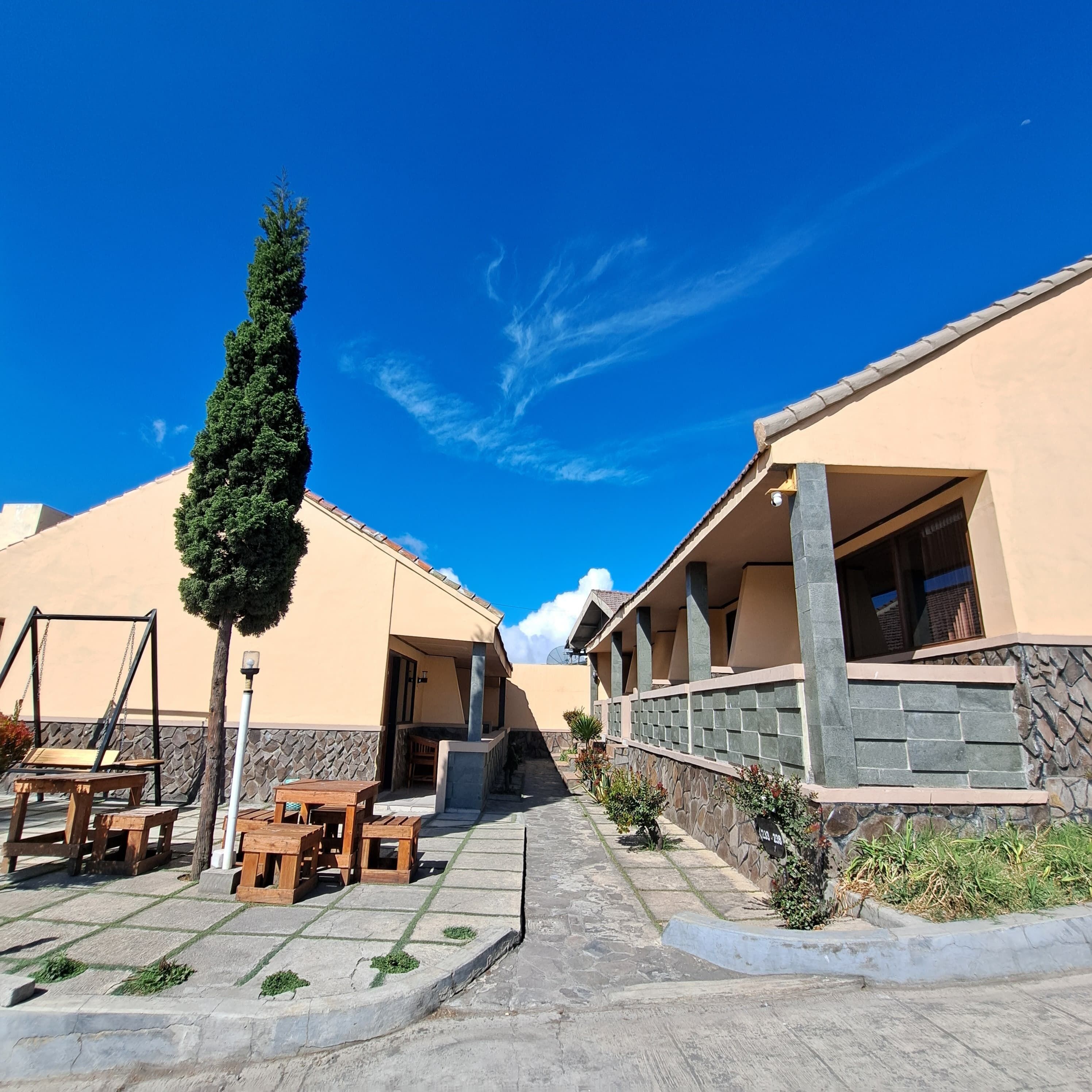 A courtyard with two beige buildings, a wooden swing set, and a tall tree.