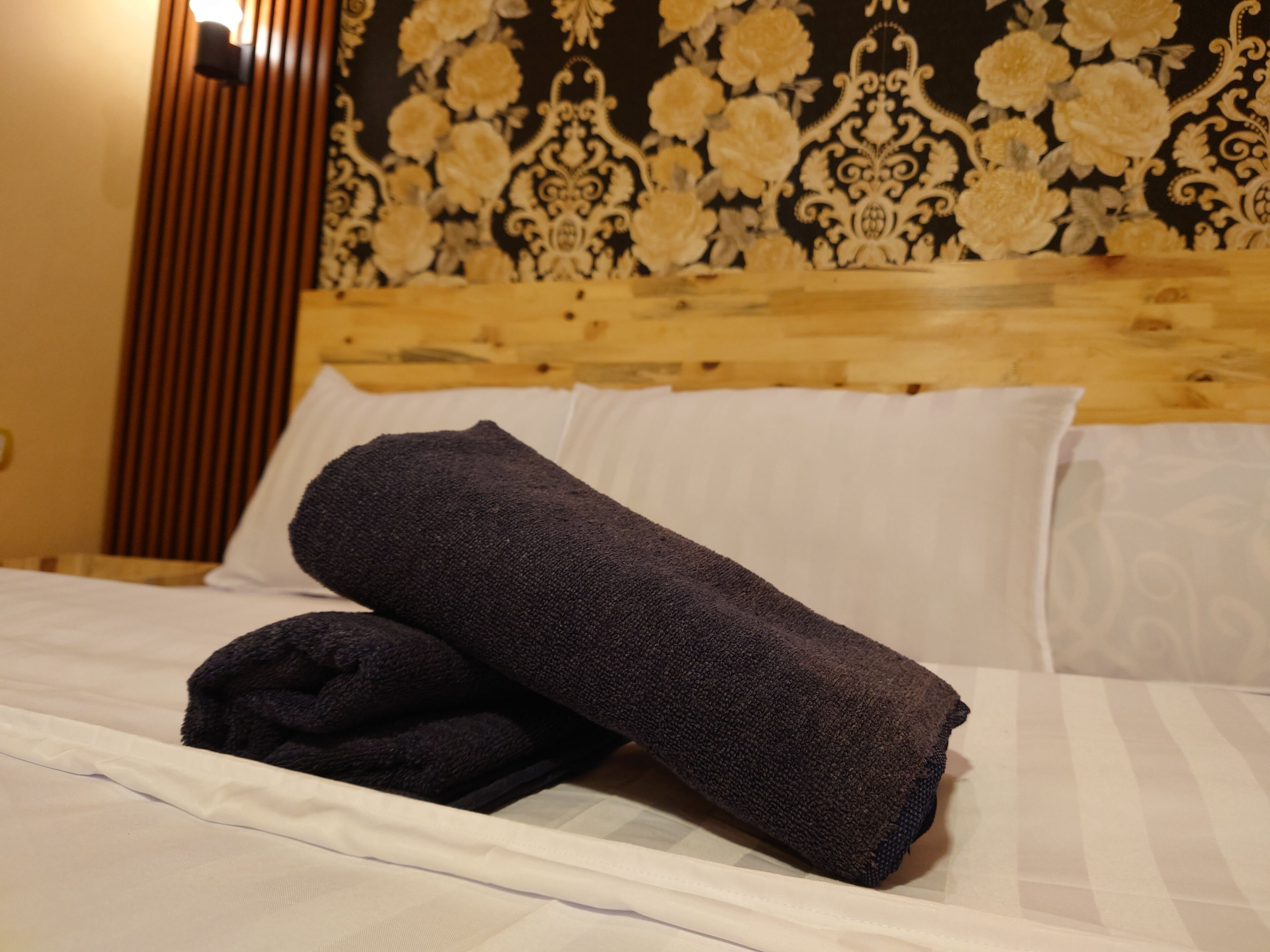 A neatly made bed with a rolled-up dark towel and a white pillow.