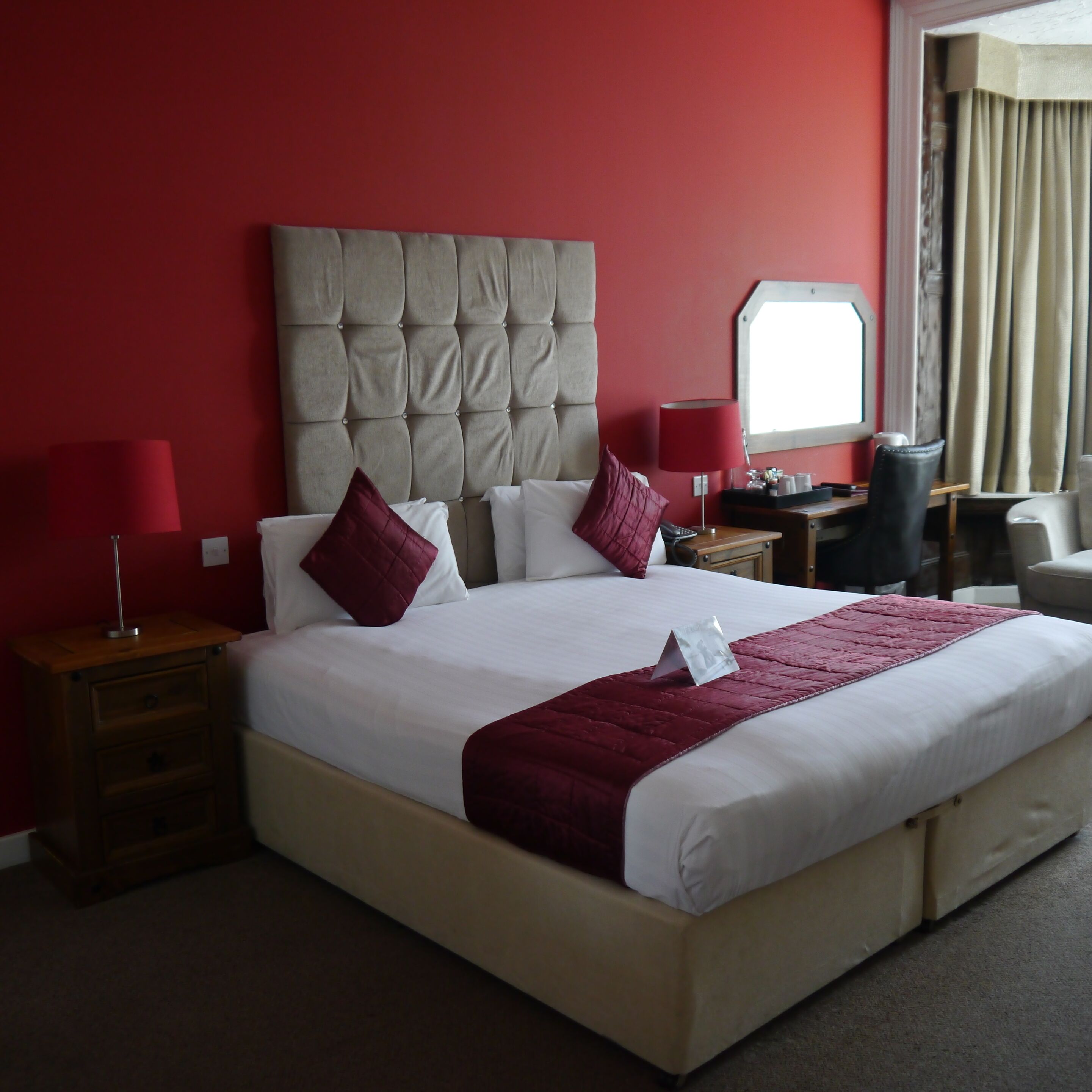 A hotel room with a large bed, red walls, and a window with curtains.