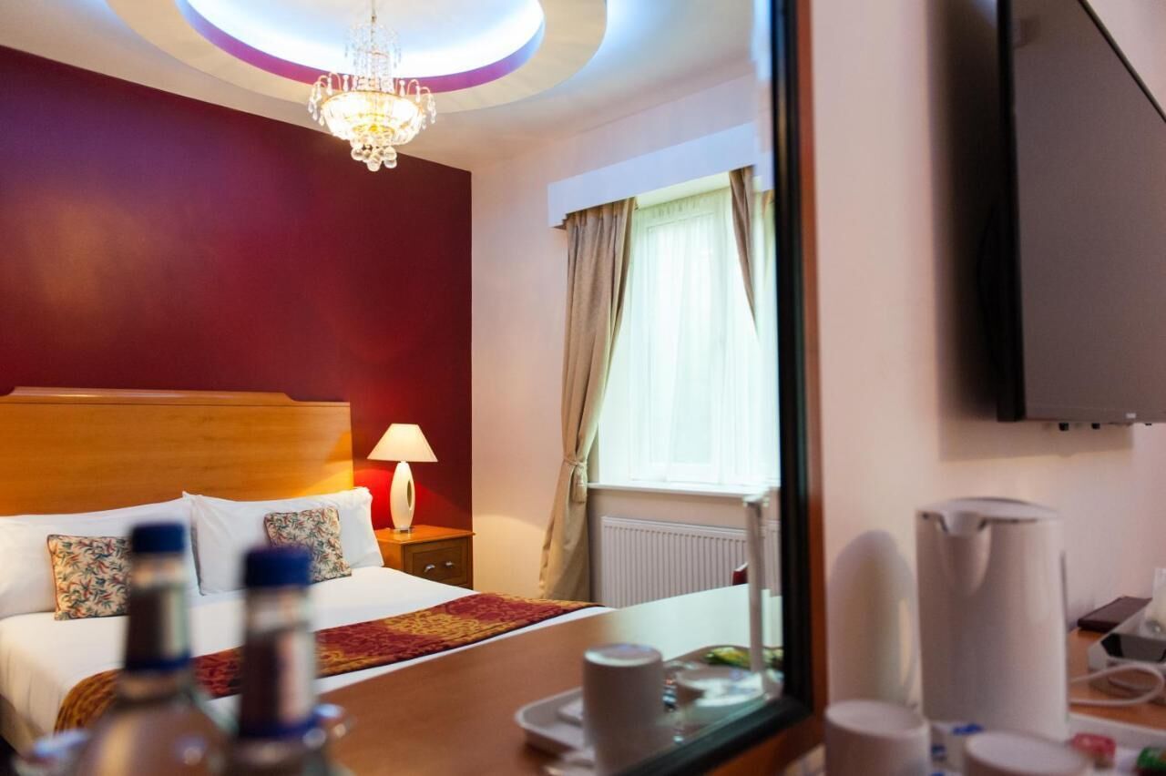 A hotel room with a wooden bed, a chandelier, a TV, and a window with curtains.