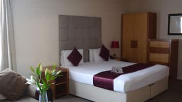 A hotel room with a large bed, a nightstand, a dresser, and a small table with a vase of flowers.