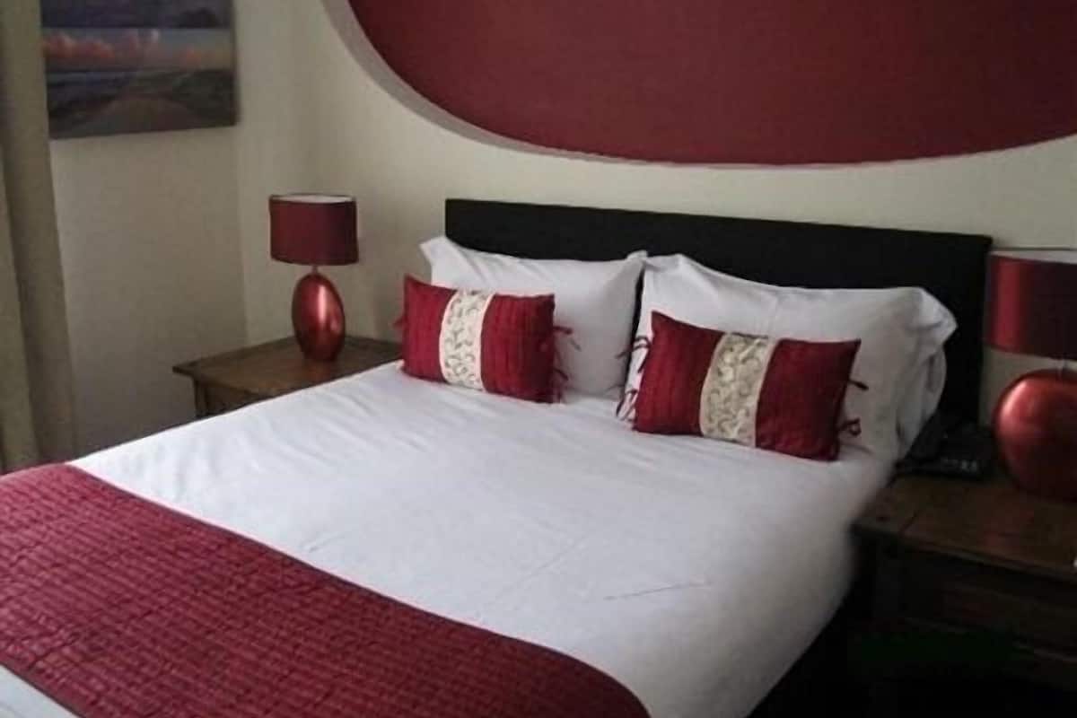 A neatly made bed with white and red bedding, a dark headboard, and two bedside lamps.