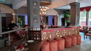 Un restaurant doté d’un bar central, de plusieurs types de sièges, notamment des banquettes et des tables rondes, et d’un plafond décoratif agrémenté de luminaires suspendus.