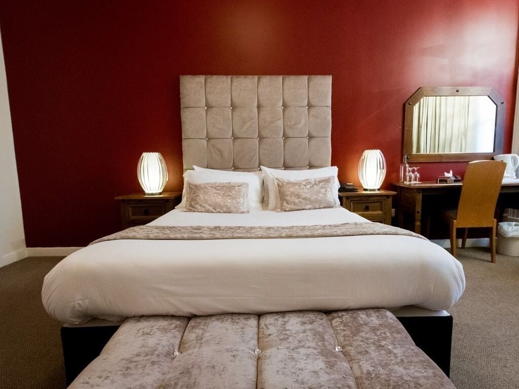 A hotel room with a large bed, two bedside tables, a chair, and a desk with a mirror.