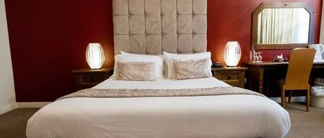 A hotel room with a large bed, two bedside tables, a chair, and a desk with a mirror.
