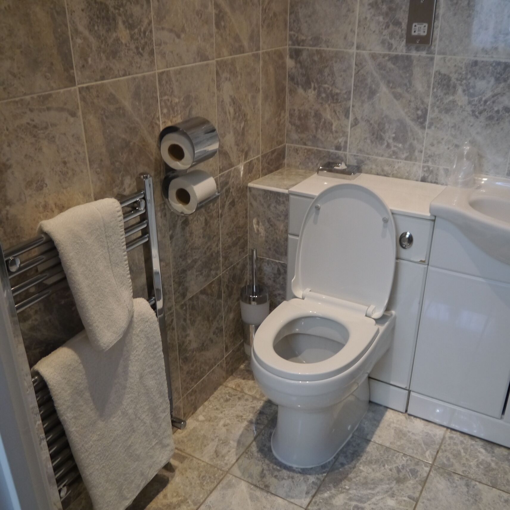 A bathroom with a toilet, a towel rack, and two rolls of toilet paper on the wall.