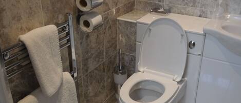 A bathroom with a toilet, a towel rack, and two rolls of toilet paper on the wall.