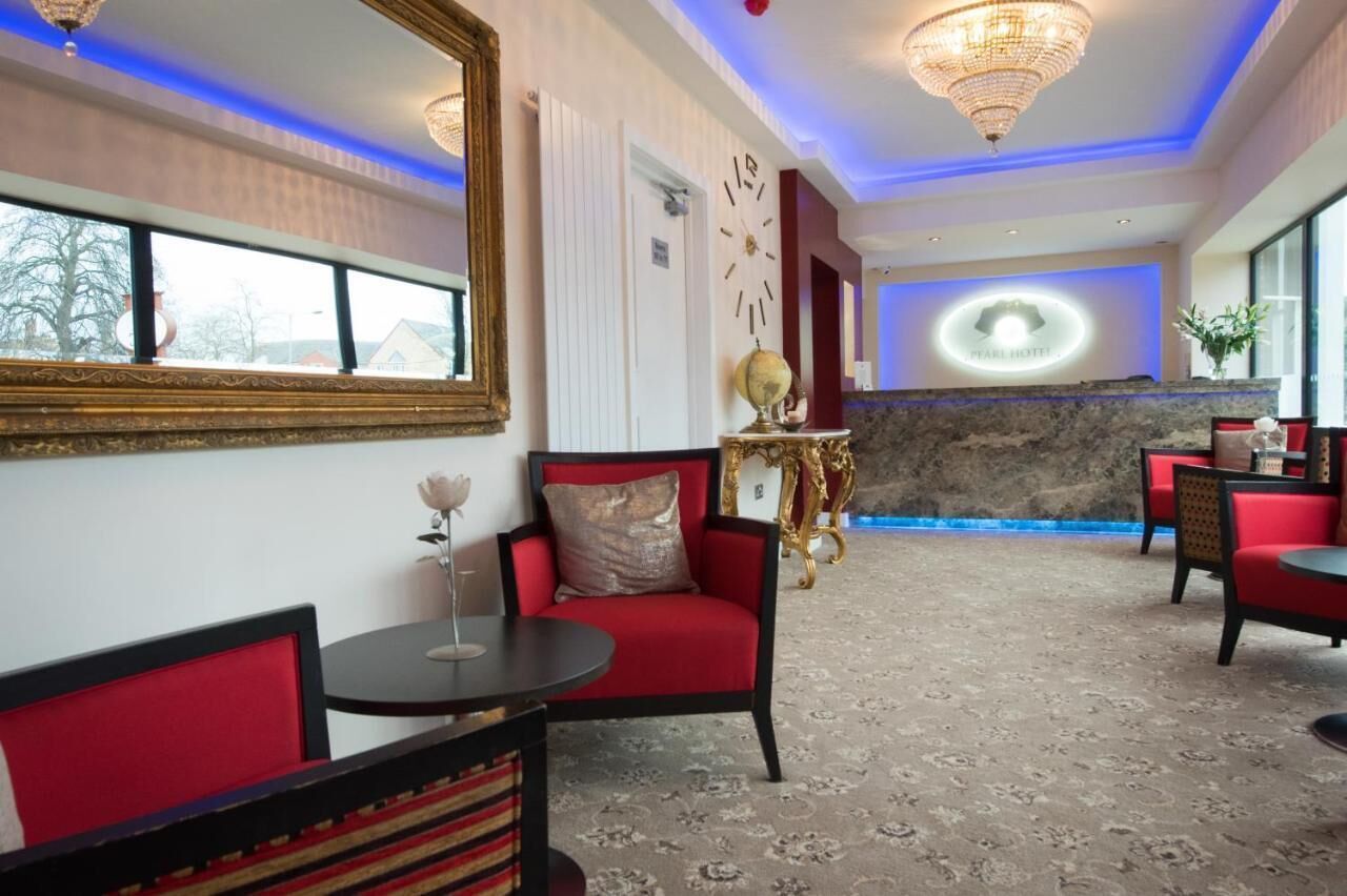 Een hotel lobby met rode en zwarte zitplaatsen, een grote spiegel, een wereldbol en een klok aan de muur.