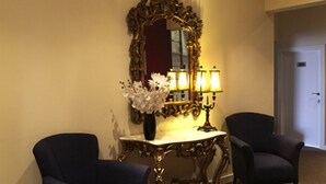 Une pièce comprenant deux fauteuils bleu foncé, un miroir doré orné, un vase blanc avec des fleurs et une table avec une lampe.