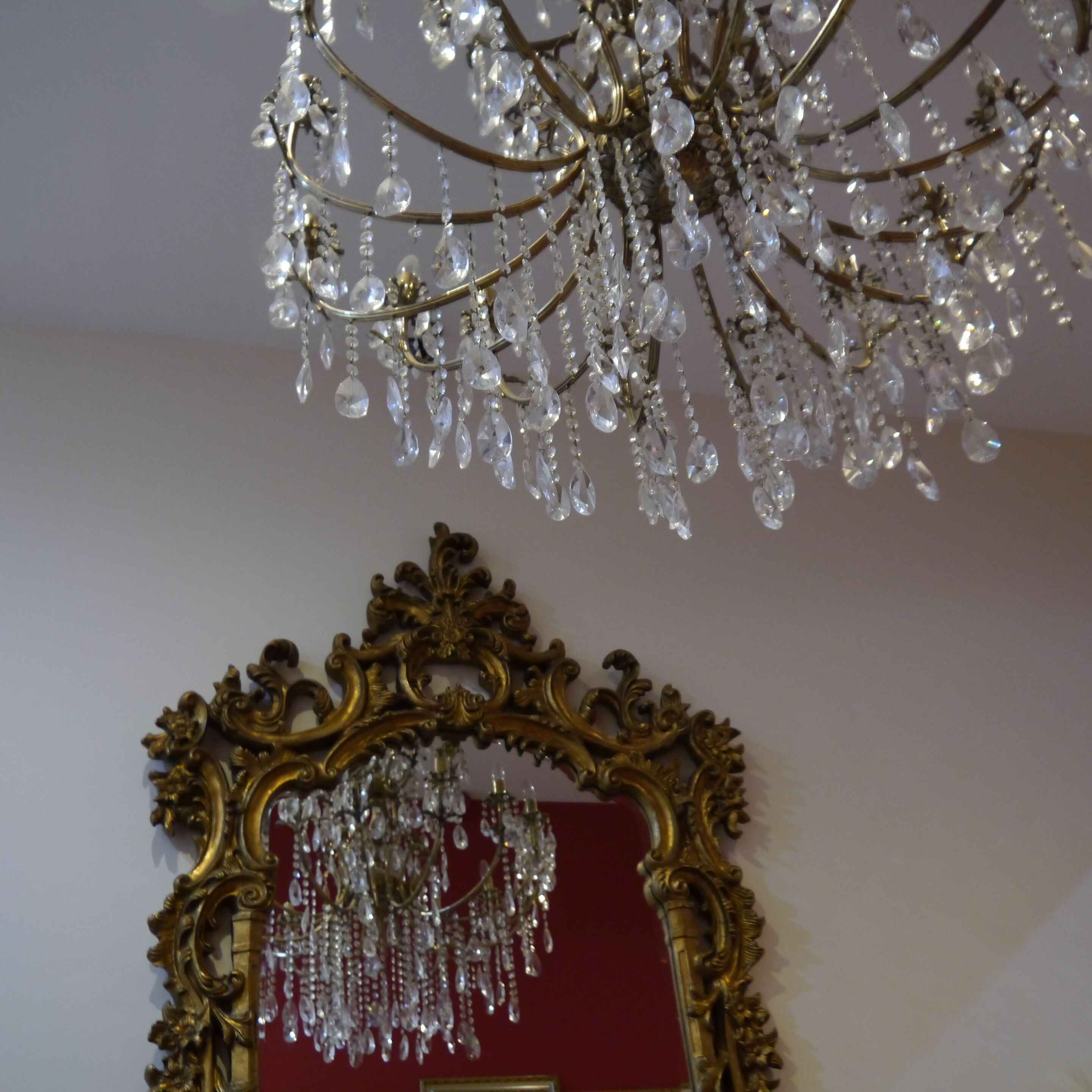 A chandelier with multiple crystal elements and a gold ornate mirror frame.