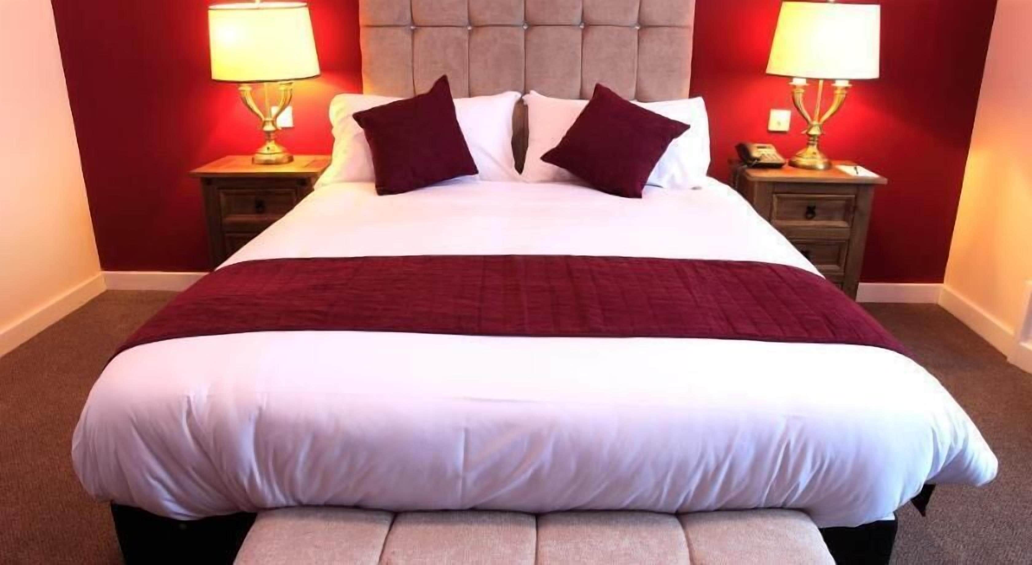 A large bed with a red blanket, two nightstands with lamps, and a tufted headboard.