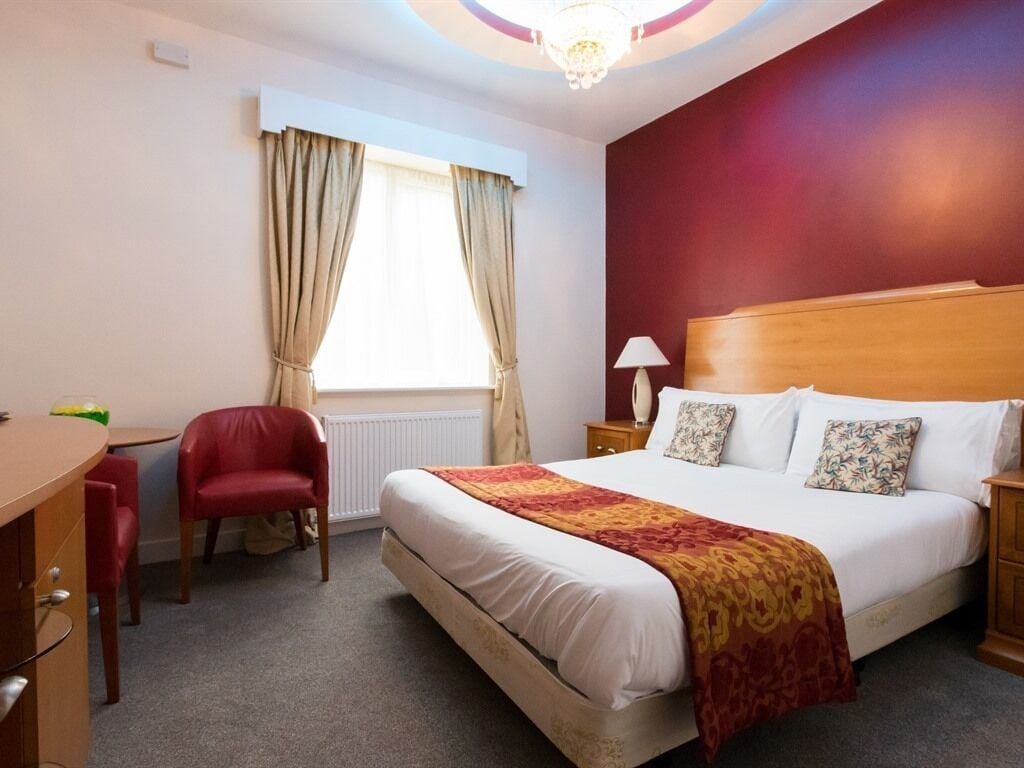 A hotel room with a bed, a desk, a chair, a lamp, and a window with curtains.