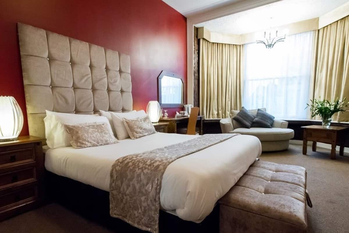A hotel room with a large bed, a desk, a chair, and a small table.