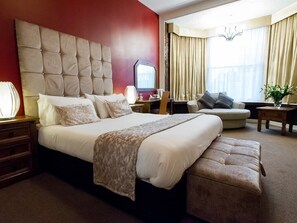 A hotel room with a large bed, a desk, a chair, and a small table.