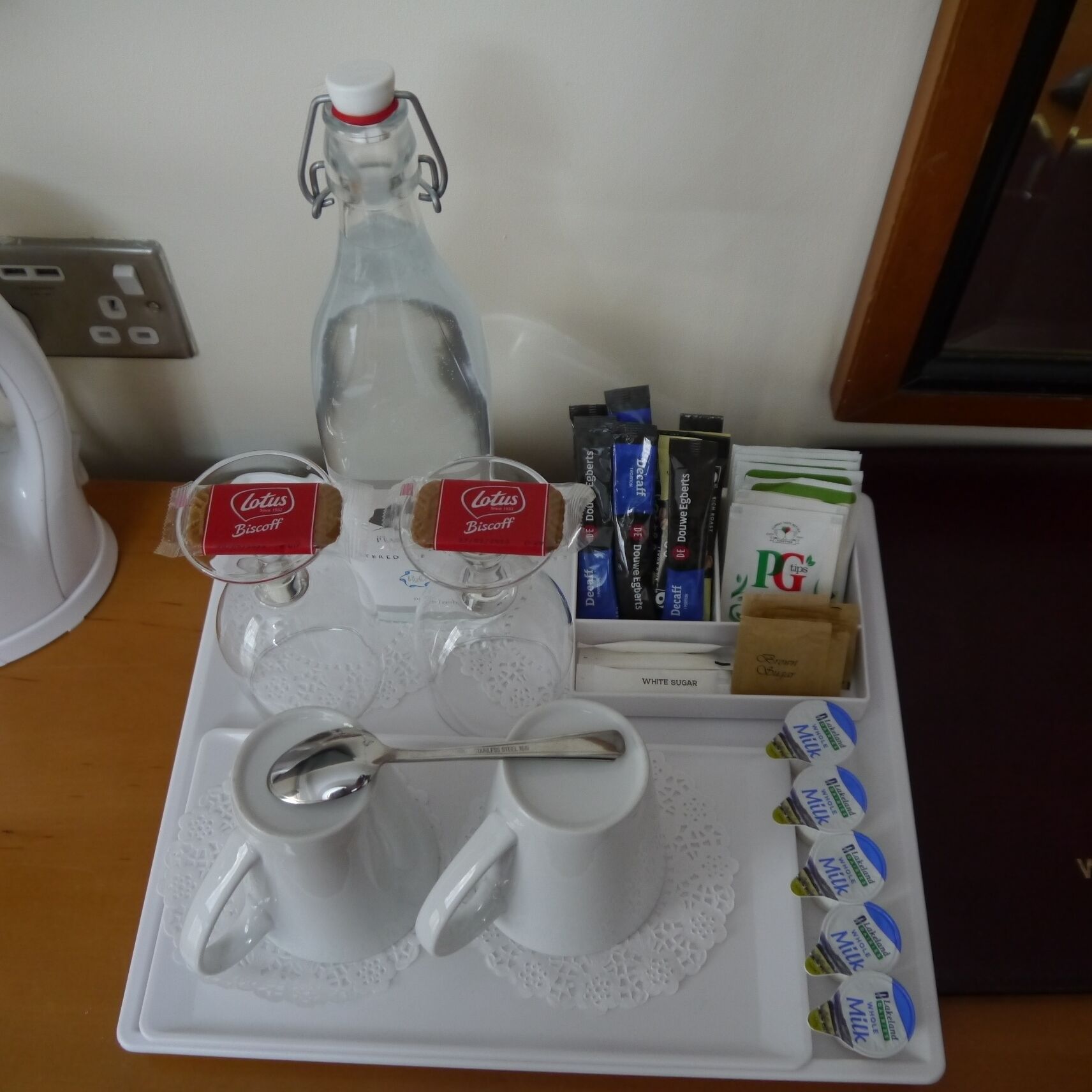 Una bandeja con una botella de agua, dos tazas de café, sobres de azúcar y una cuchara.