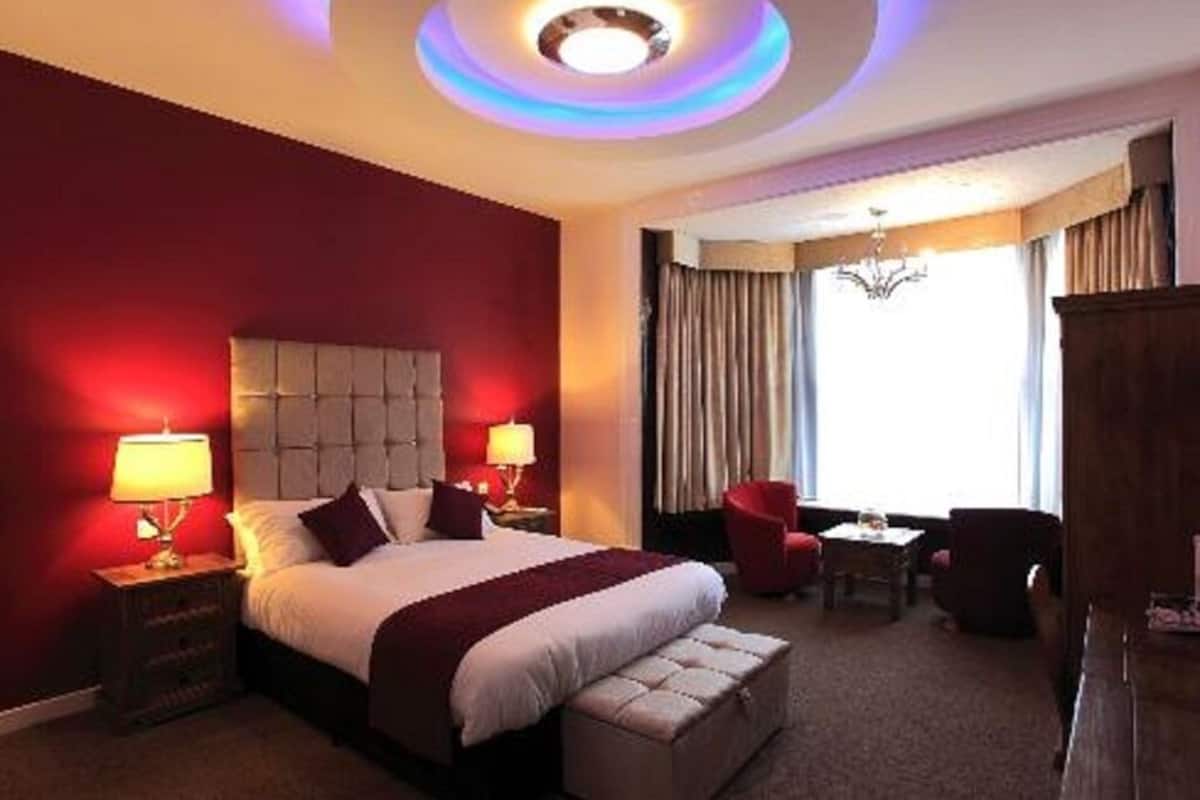 A hotel room with a large bed, two bedside tables with lamps, a red armchair, a small table, and a view of the outdoors.