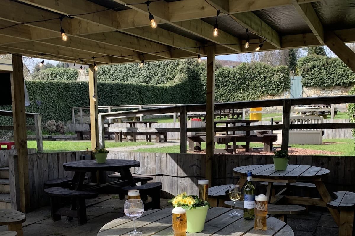 An outdoor patio area with wooden tables and benches, surrounded by a wooden fence.