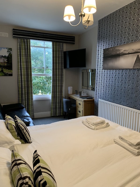 A hotel room with a bed, a desk, a chair, a TV, and a window with curtains.