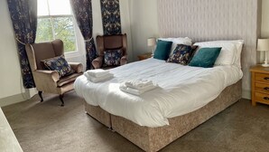 Un dormitorio ordenado con una cama grande, una silla y una mesita de noche.
