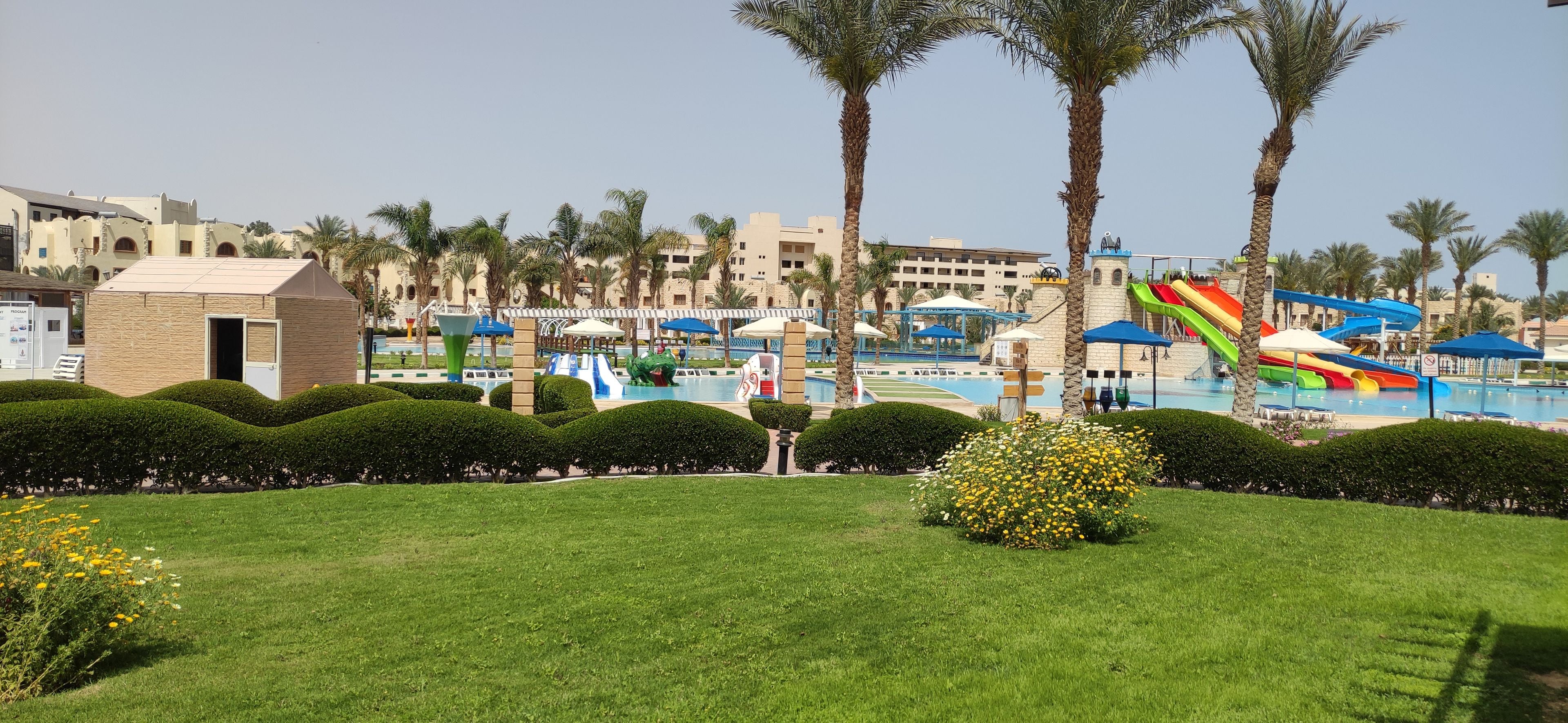 A resort with a swimming pool, water slides, palm trees, and a small building.
