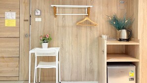 Una cocina compacta con pared de madera, una mesa blanca con una silla, un perchero, un refrigerador pequeño y una planta en maceta.