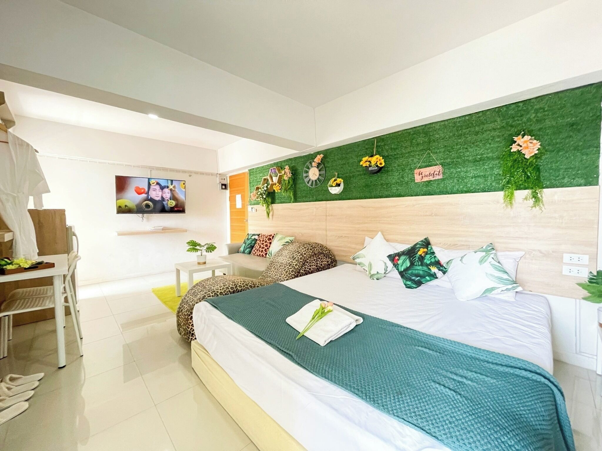 Un dormitorio moderno con cama, televisión, escritorio y pared verde con flores.