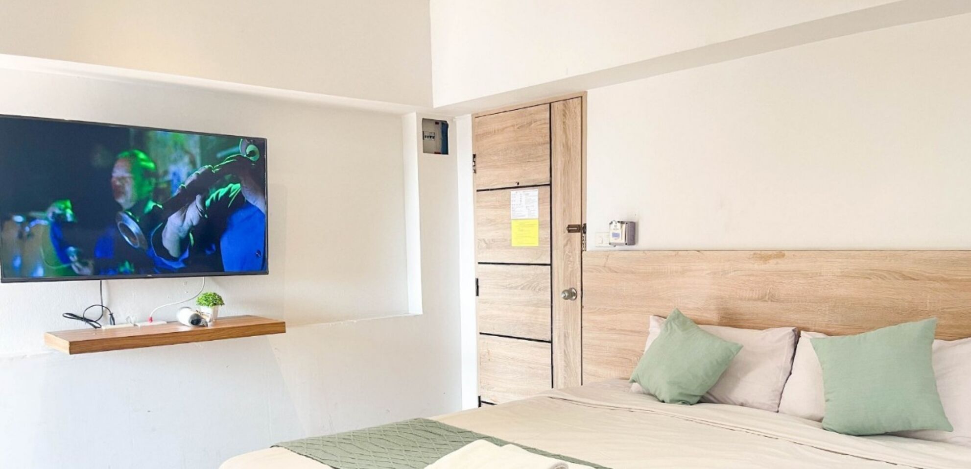 A bedroom with a TV mounted on the wall, a wooden headboard, and a bed with pillows.