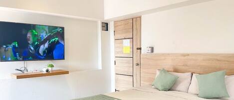 A bedroom with a TV mounted on the wall, a wooden headboard, and a bed with pillows.