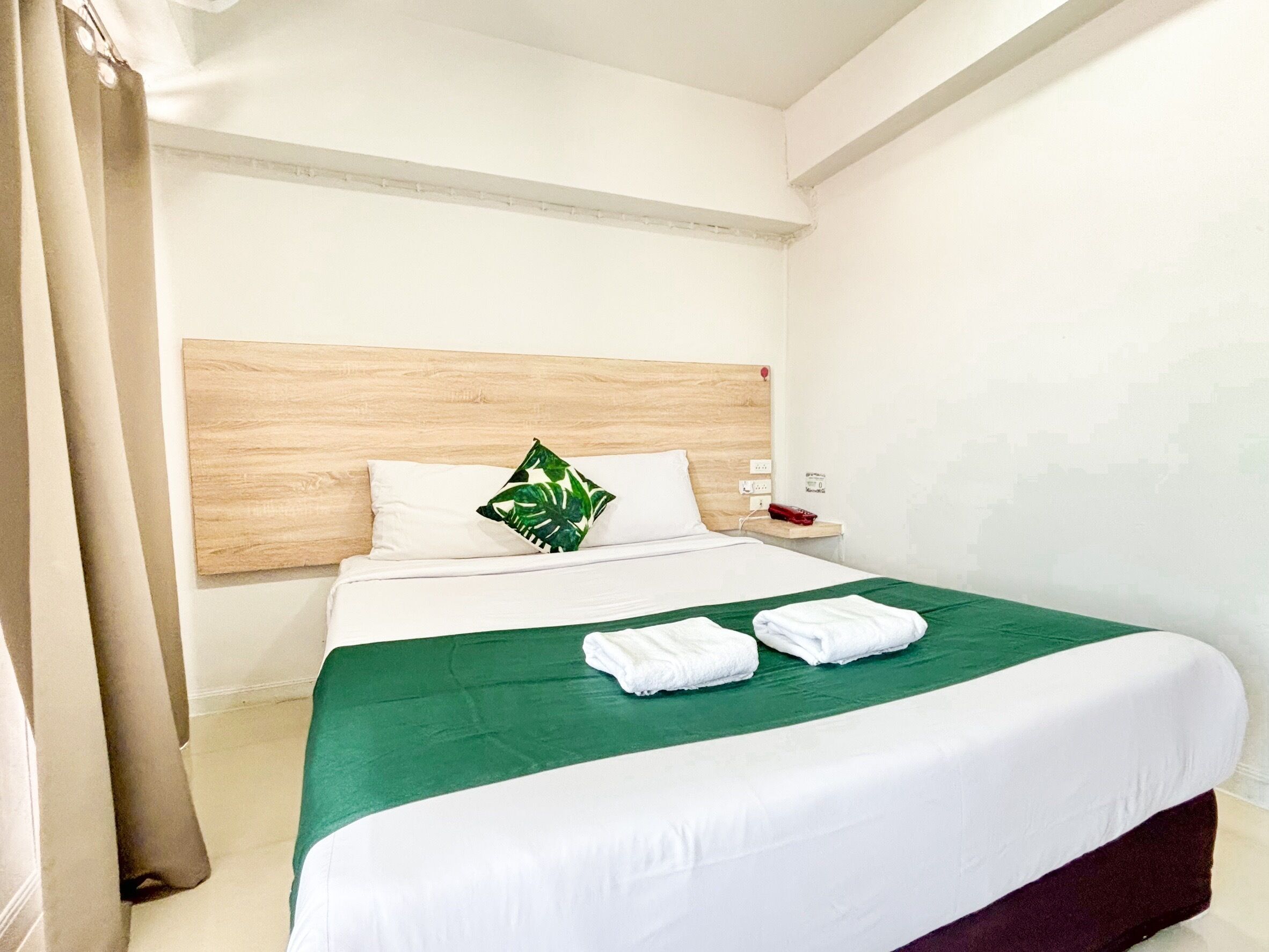 A hotel room with a wooden headboard, a green bedspread, white bedding, and neatly folded towels on the bed.