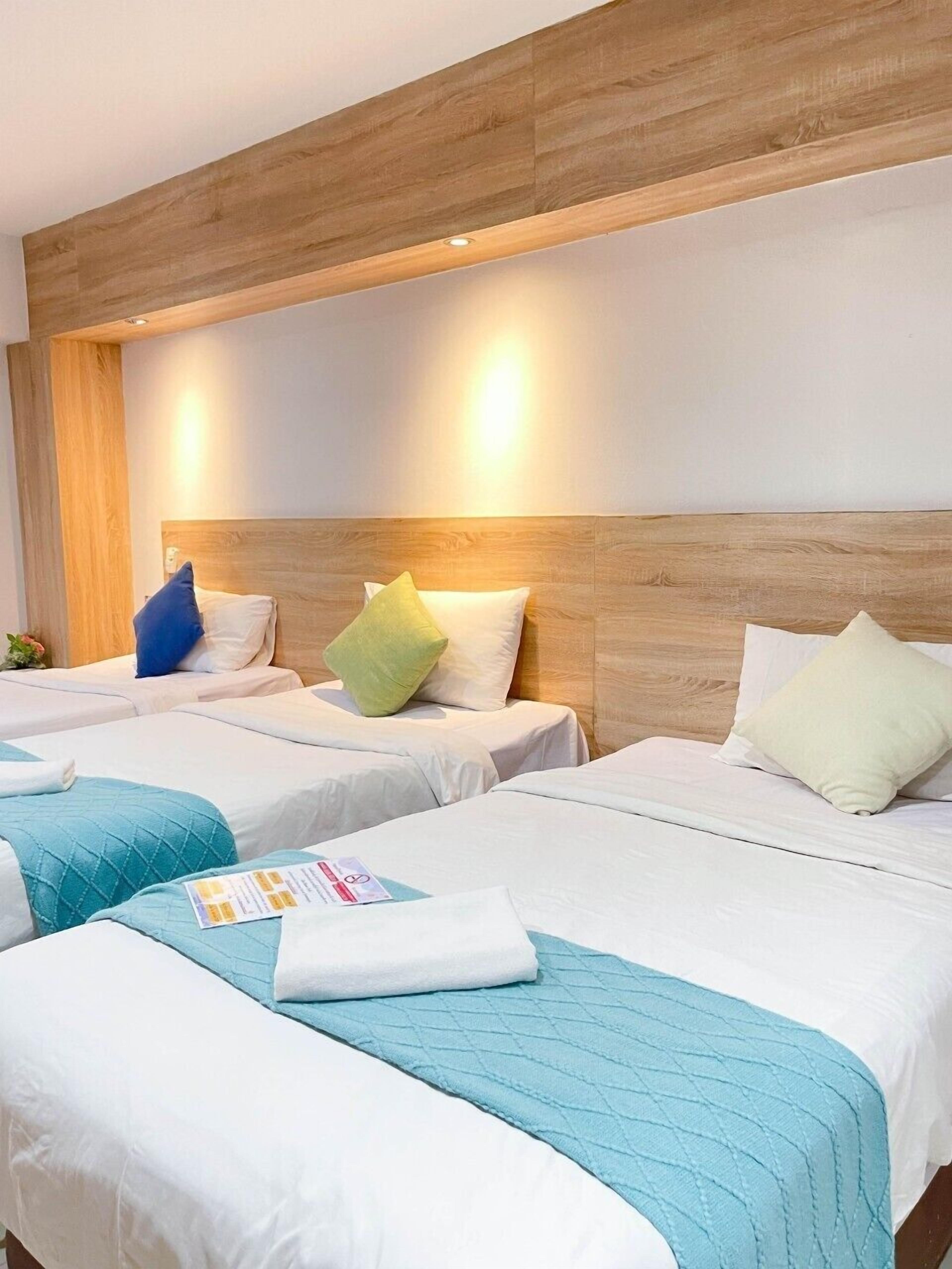 Een hotelkamer met twee bedden, elk voorzien van een houten hoofdbord, wit beddengoed en een teal geborduurd plaid.