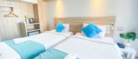 A hotel room with two beds, each with a blue quilted bedspread and white pillows. There is a wooden headboard, a bedside table with a phone, and a small plant on the nightstand.