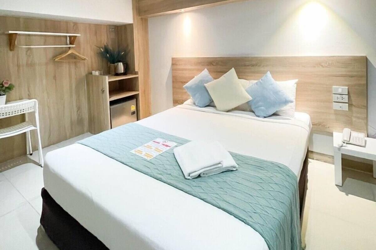 A modern hotel room with a large bed, bedside tables, a wardrobe, and a small desk with a chair.