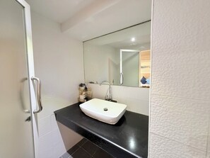 Une salle de bain moderne avec un lavabo blanc, un grand miroir et un plan de toilette noir.