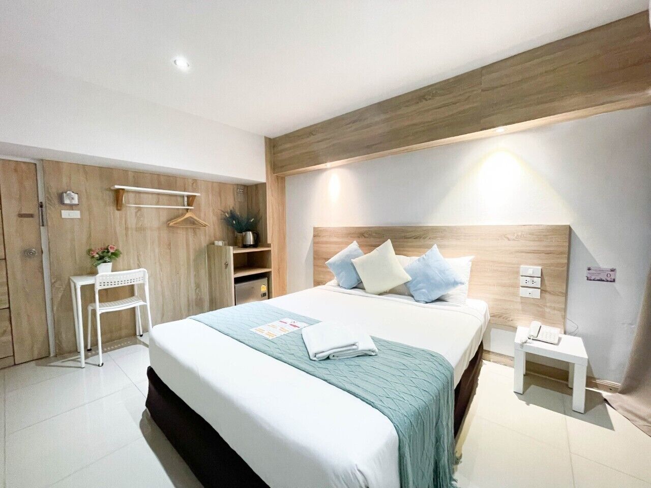 A modern bedroom with a large bed, bedside tables, a wardrobe, and a small desk with a chair.