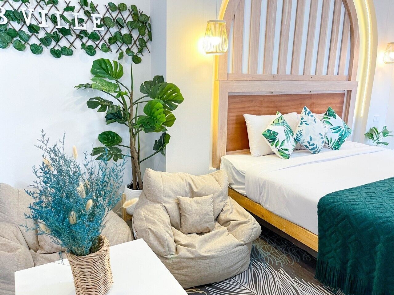A bedroom with a bed, a bedside table, a chair, a potted plant, and a wall-mounted light fixture.