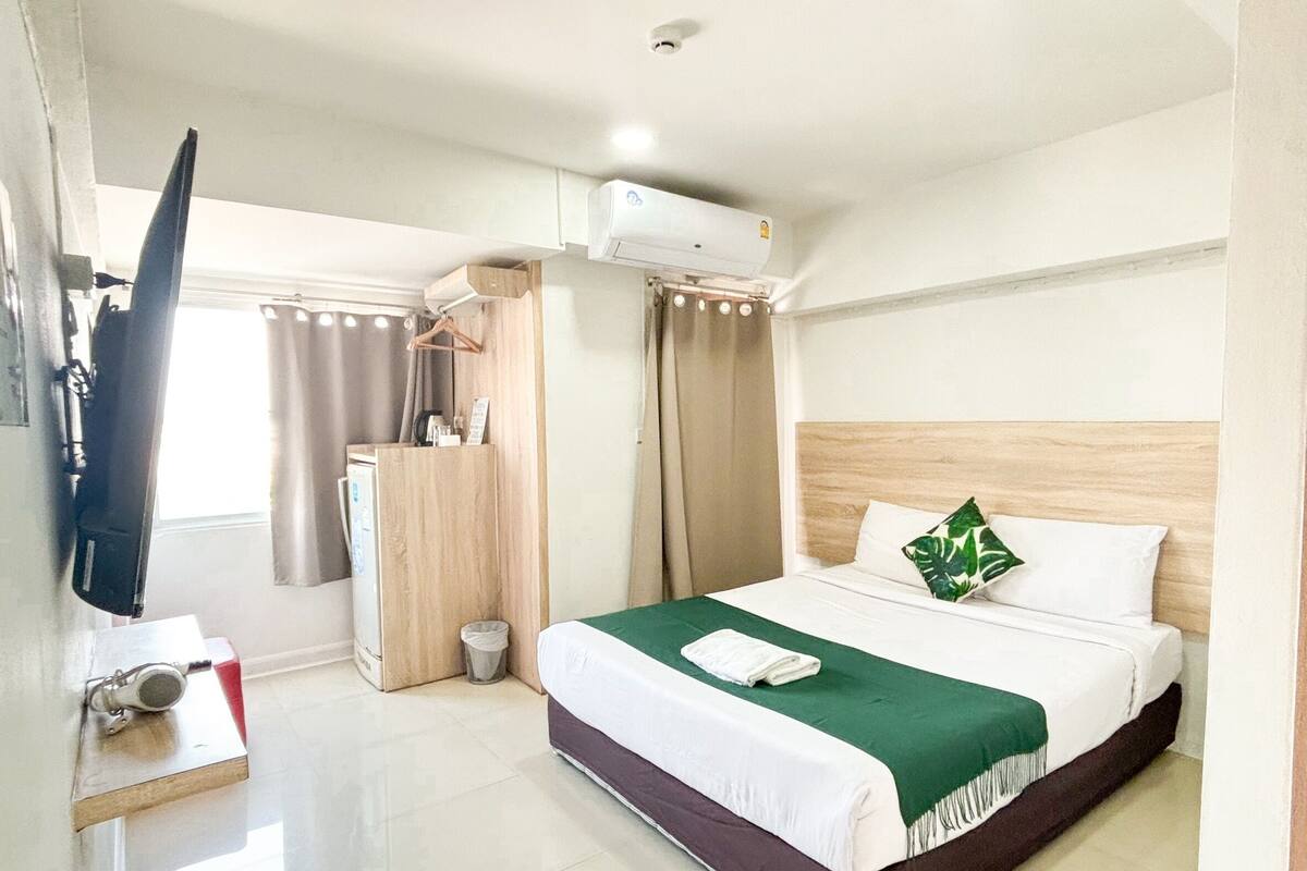 A hotel room with a bed, a TV, a desk, and an air conditioning unit.