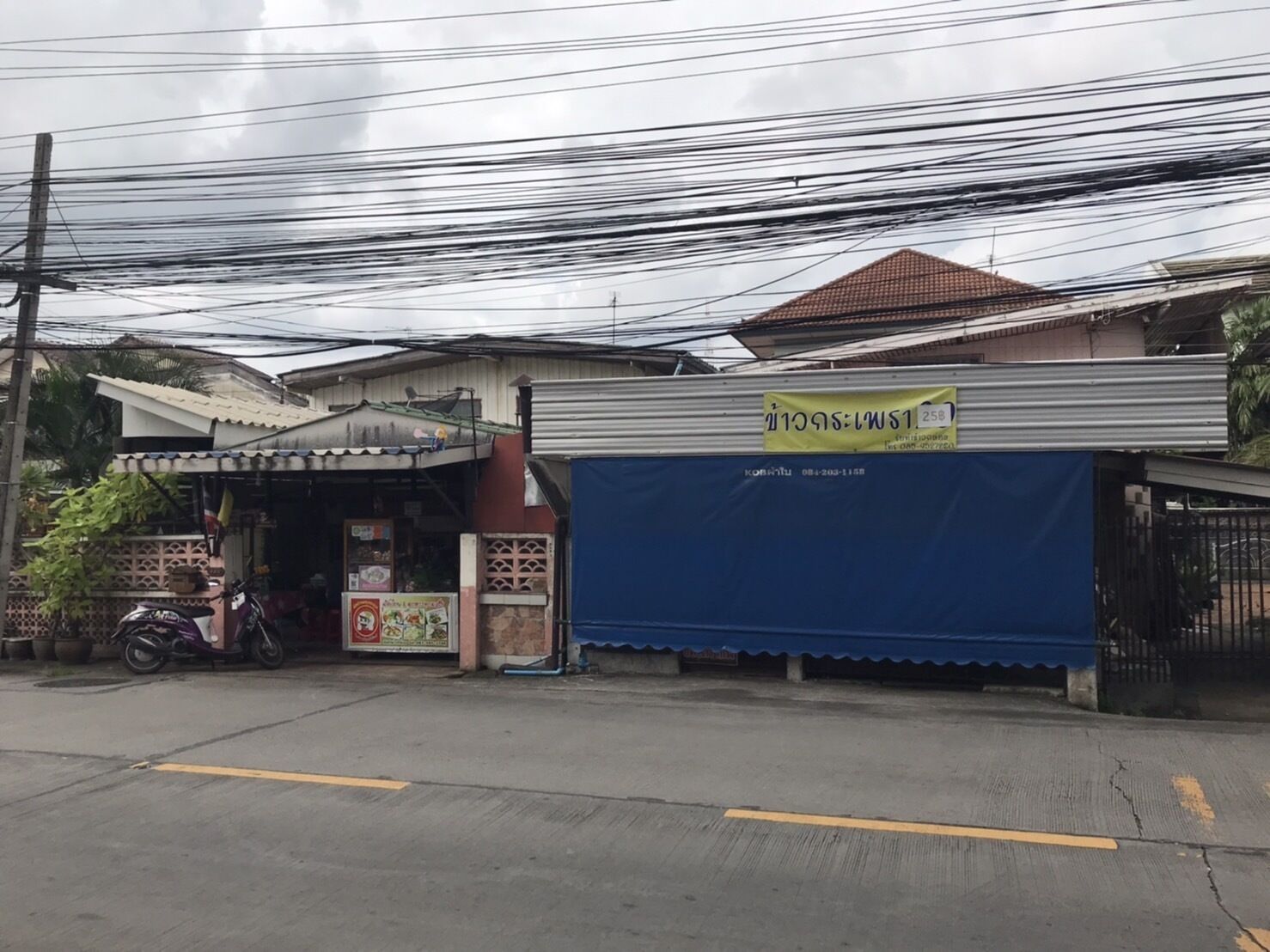 A small roadside shop with a blue awning, a motorcycle parked in front, and a signboard above the entrance.