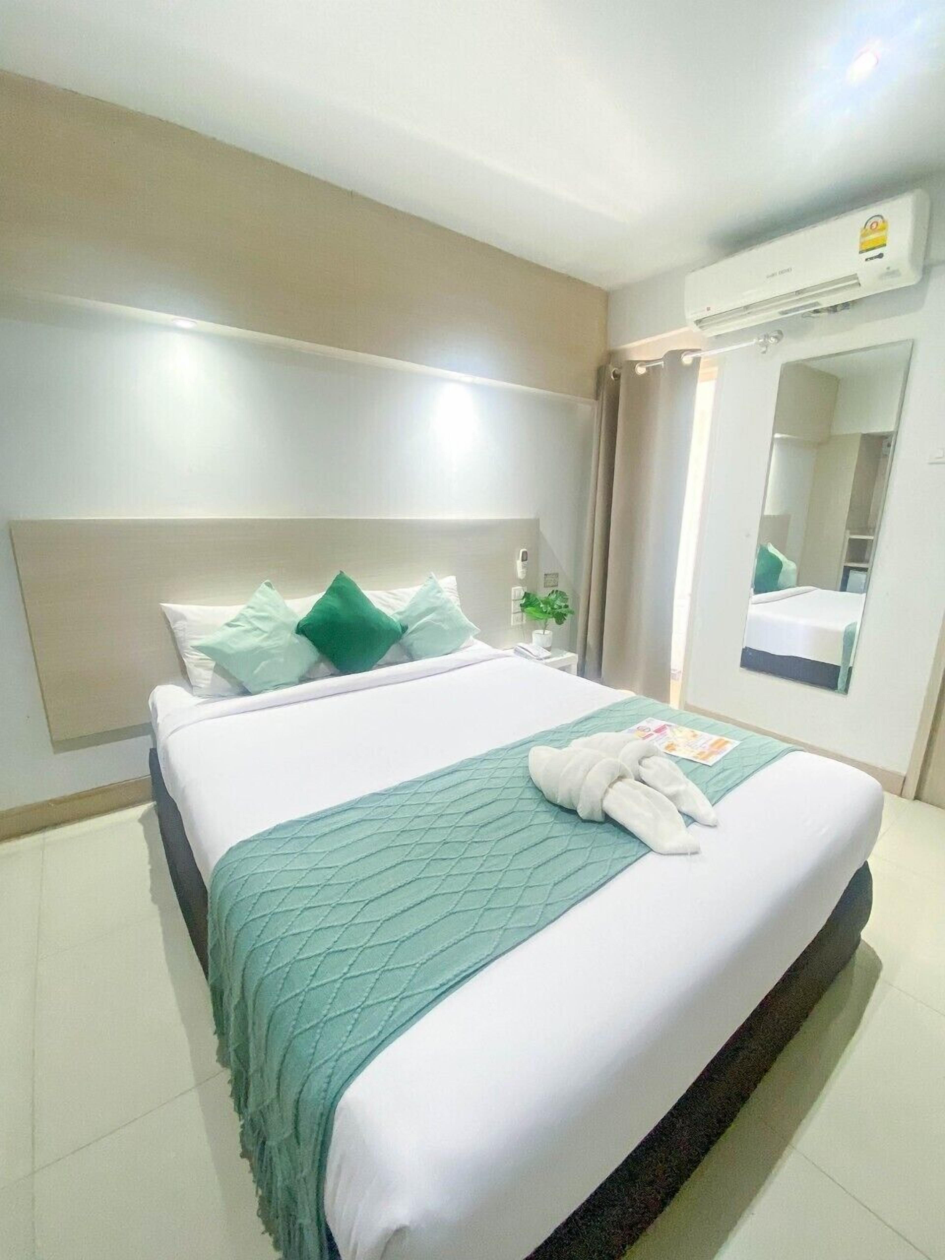 Een hotelkamer met een groot bed, een nachtkastje, een spiegel en een wandgemonteerde airconditioning.