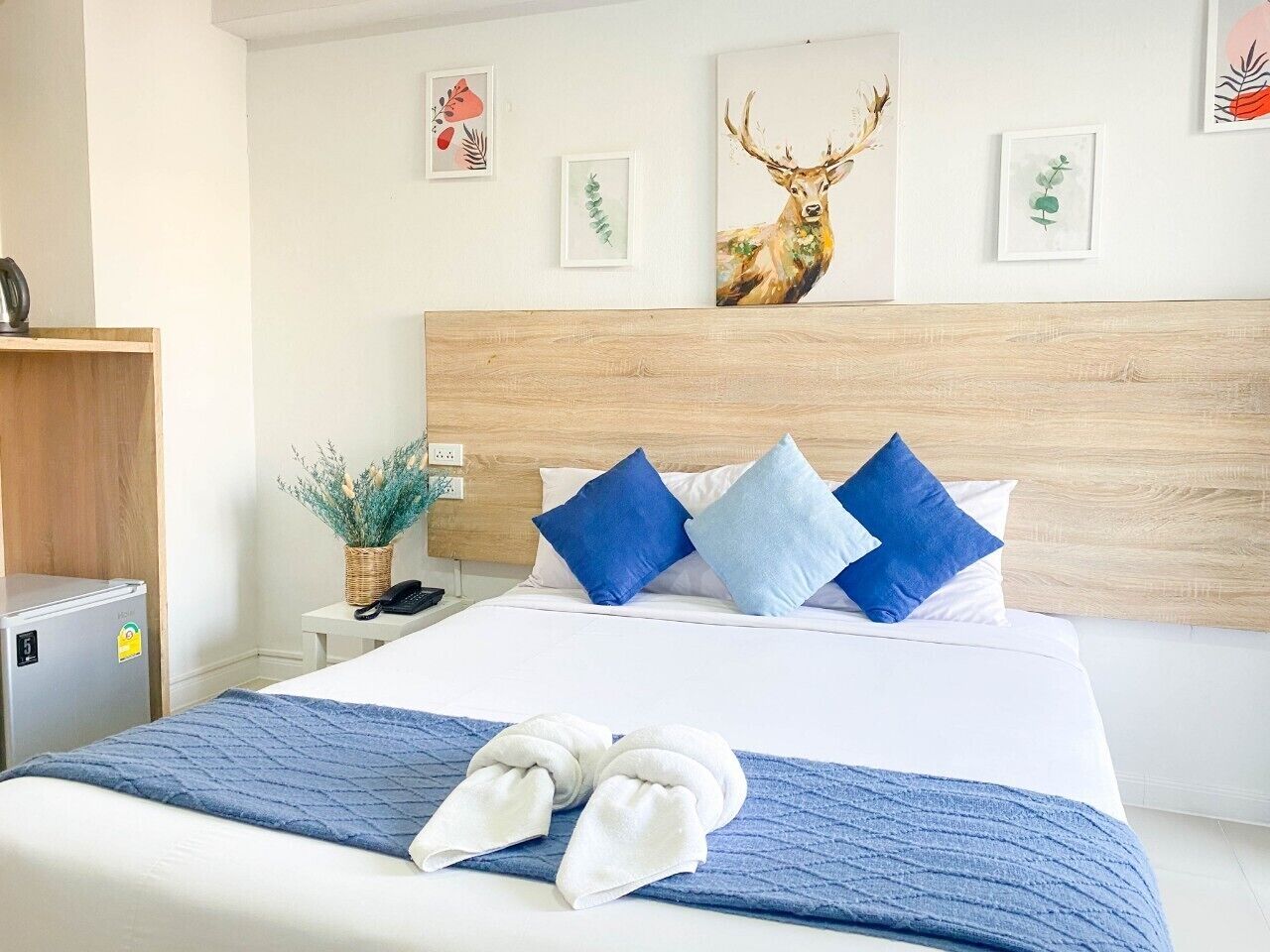 A hotel room with a bed, blue and white pillows, a wooden headboard, and a wall with framed artwork.