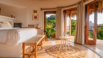 A spacious bedroom with a large bed, a wooden bench, a small table with a glass top, and a woven rug.
