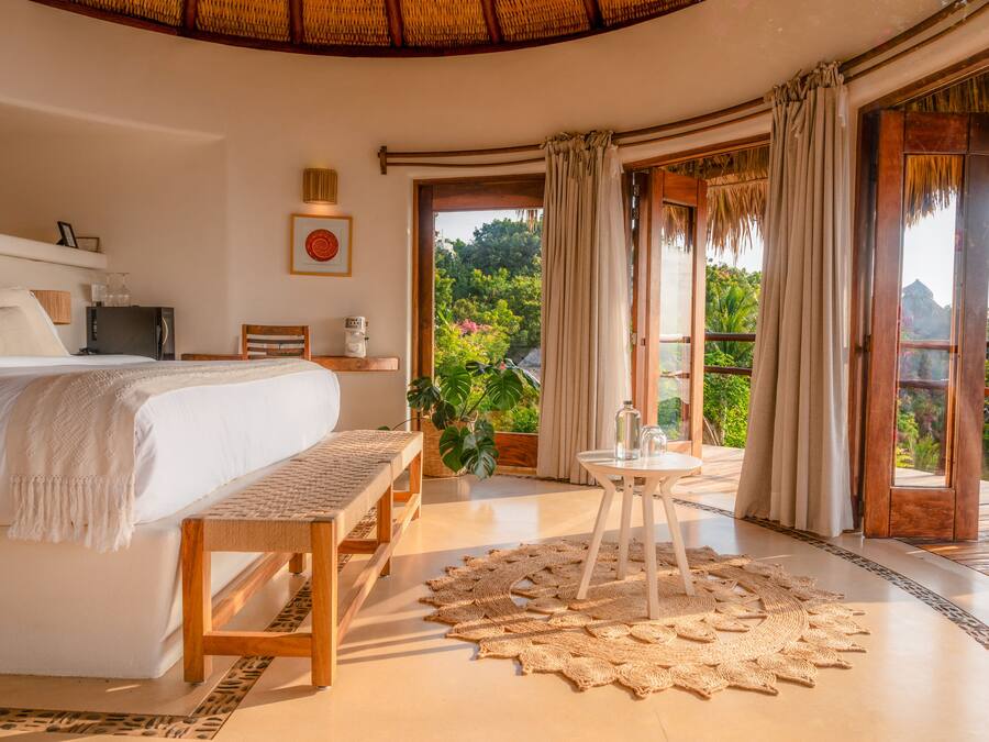 A spacious bedroom with a large bed, a wooden bench, a small table with a glass top, and a woven rug.