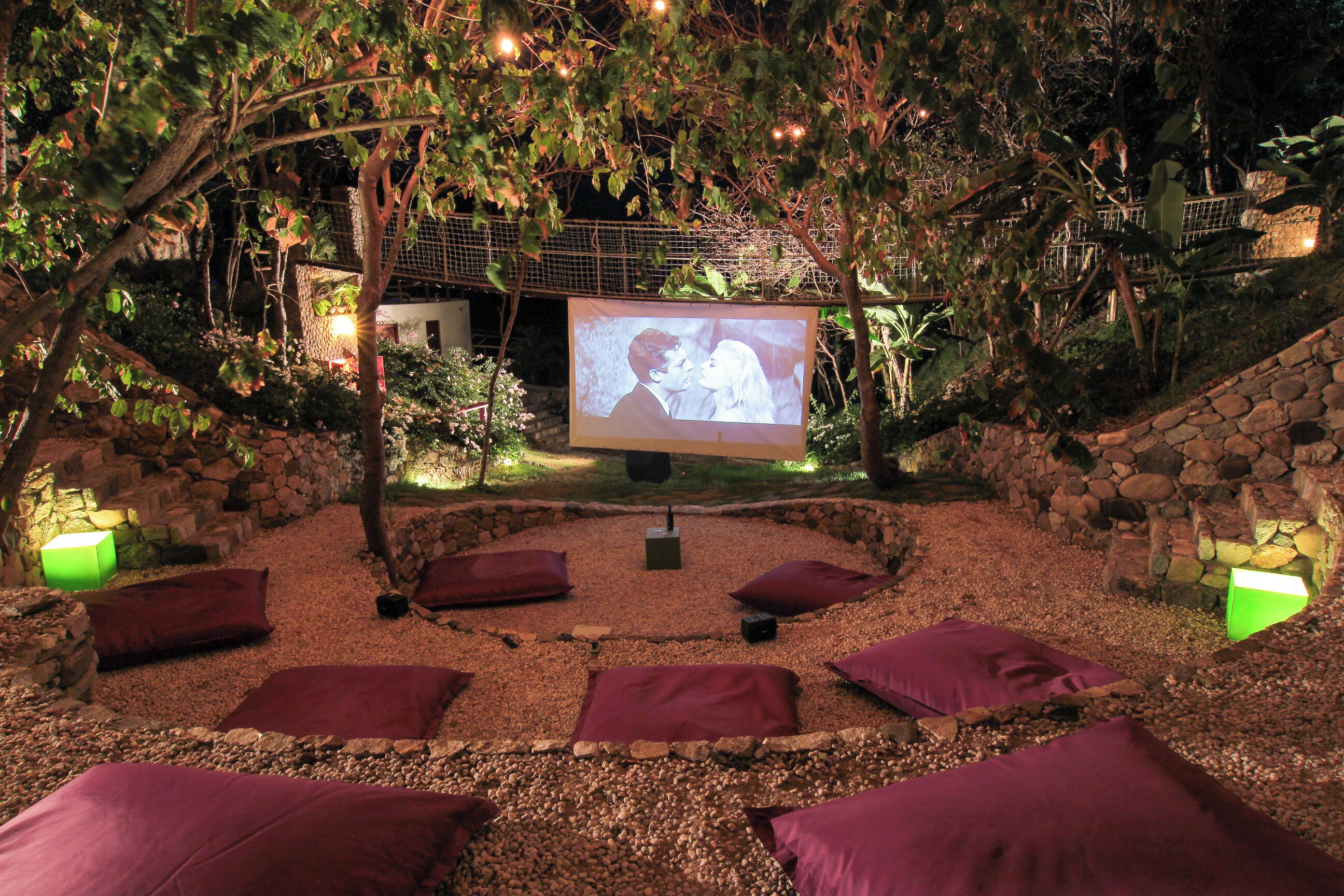 An outdoor cinema area with a screen, seating, and stone walls.
