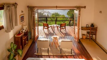 Una habitación con una cama, una mesita con sillas, un escritorio con una silla, una planta en maceta y vista al océano a través de un ventanal.