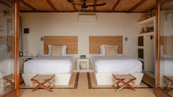 A room with two beds, a ceiling fan, a small table, and a shelf with decorative items.