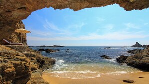 A beach with a rocky cave entrance, a lounge chair, and a clear view of the ocean.